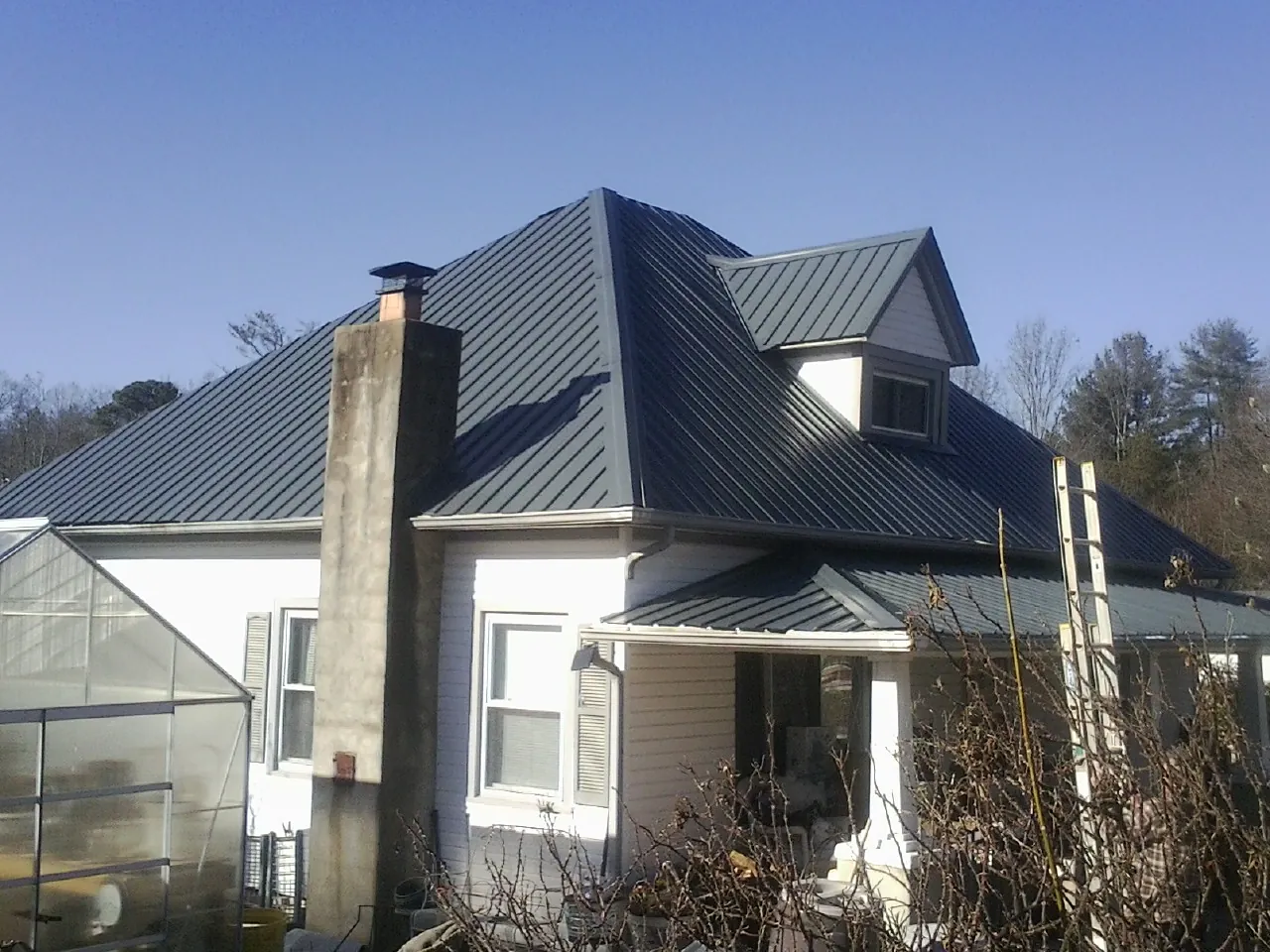 Dark blue standing seam metal roof on a white farmhouse with dormer — Slate & Tile Roof Repair by Roofing Brothers in South Wellfleet