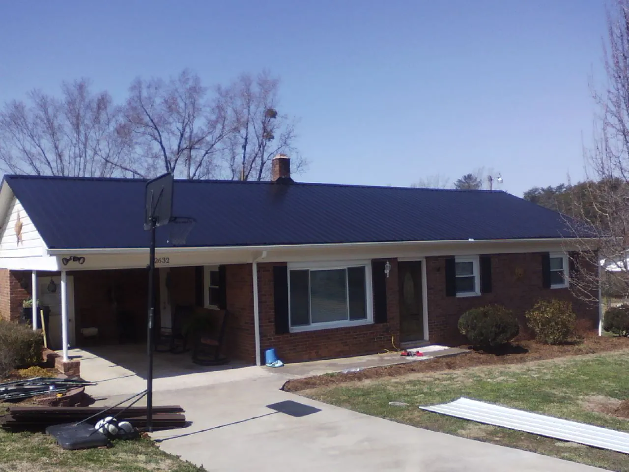 Finished dark blue metal roof on a brick ranch with a carport in South Wellfleet