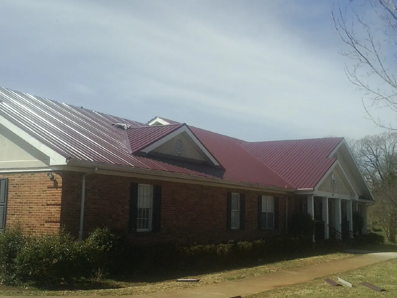 Red metal roof with gabled entries on a long brick building, from a Hail Damage Roof Repair job in South Wellfleet