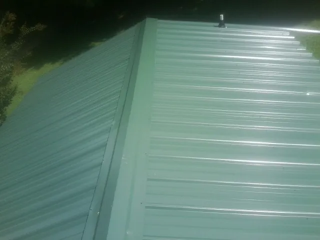 New green metal panels meeting at the ridge of a roof — Flat Roof Repair work by our crew in South Wellfleet