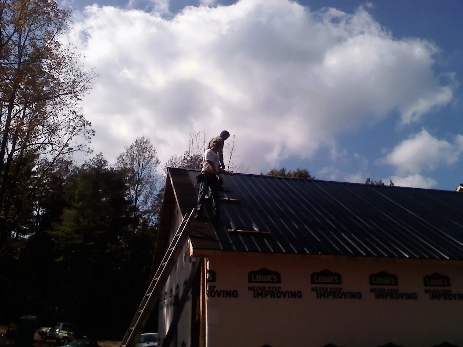 Roofer fastening dark metal panels high against a cloudy sky, from a Roof Inspection job in South Wellfleet