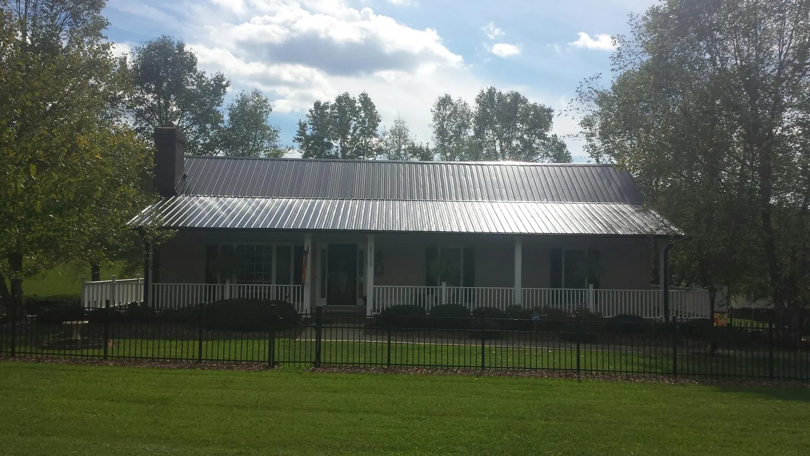 Gray metal roof on a brick ranch with a full width front porch — Gutter Guard Installation work by our crew in South Wellfleet