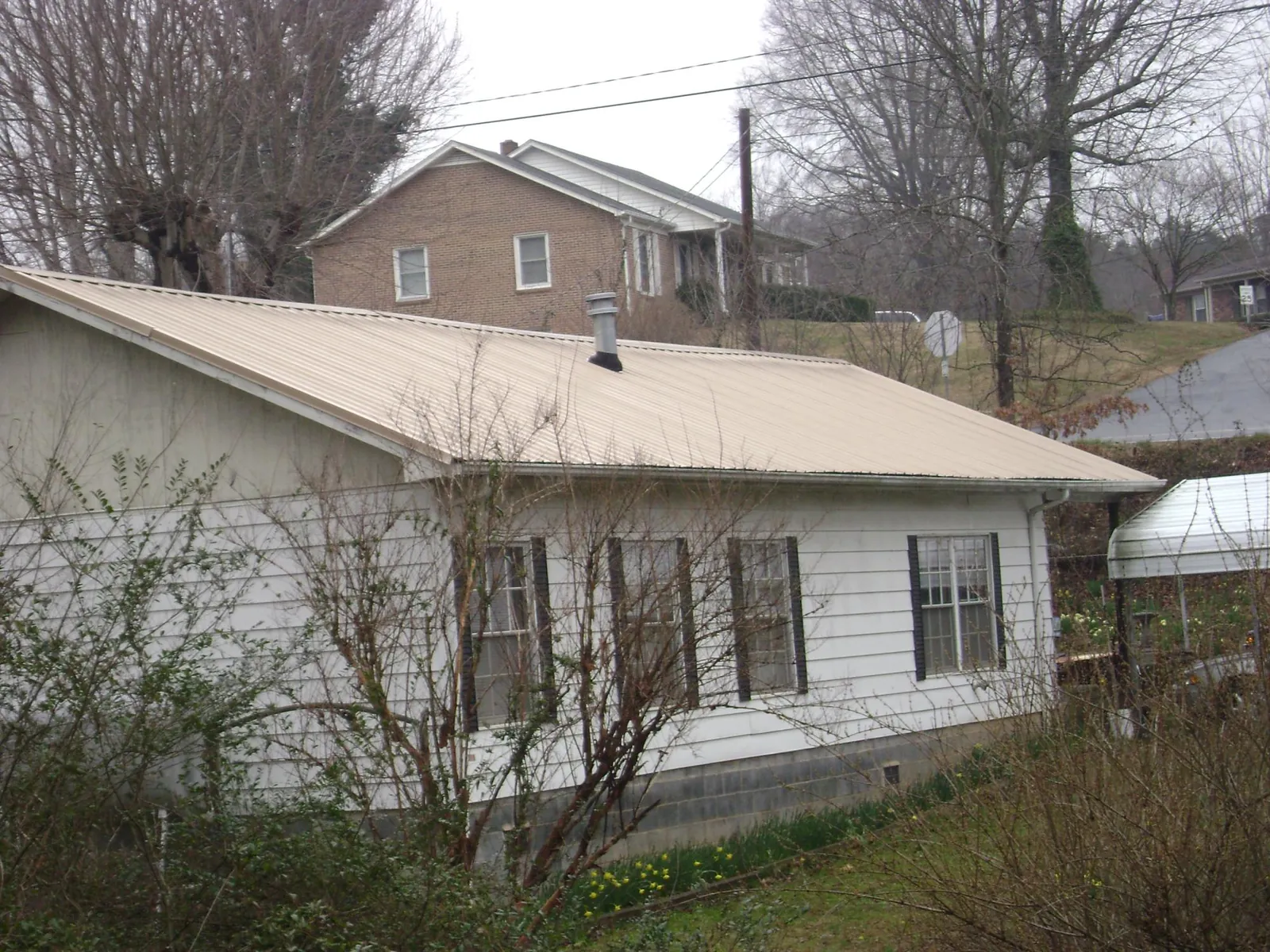 Tan metal roof on a white sided house set into a hillside — Commercial Roofing by Roofing Brothers in South Wellfleet